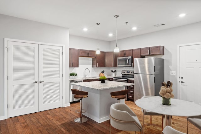 kitchen featuring dark wood-style floors, a kitchen island, a sink, stainless steel appliances, and dark brown cabinetry