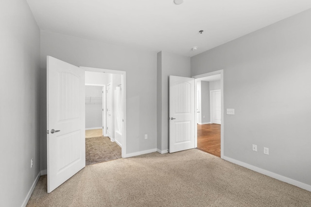 unfurnished bedroom with a closet, baseboards, a spacious closet, and carpet flooring