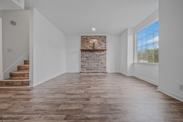 unfurnished living room with wood-type flooring and a brick fireplace