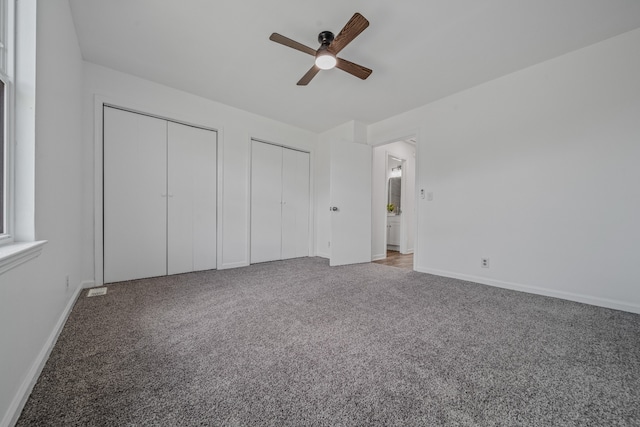 unfurnished bedroom featuring ceiling fan, carpet floors, and multiple closets