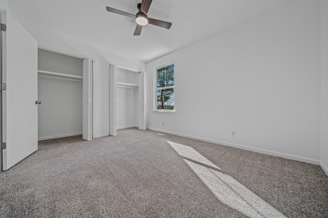 unfurnished bedroom featuring ceiling fan, carpet, and two closets