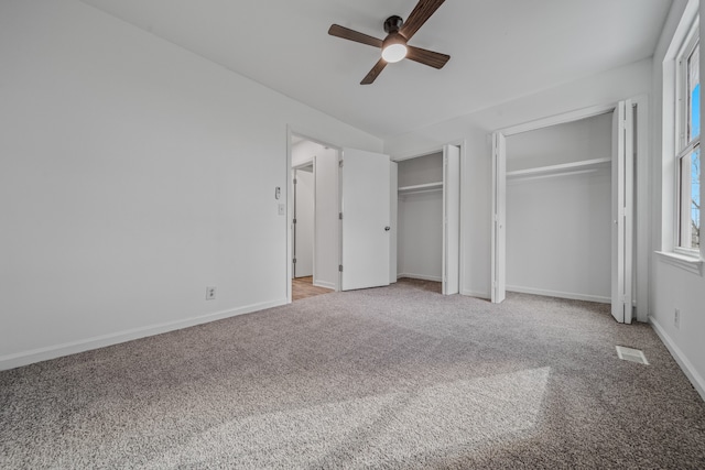 unfurnished bedroom featuring ceiling fan, light colored carpet, and two closets