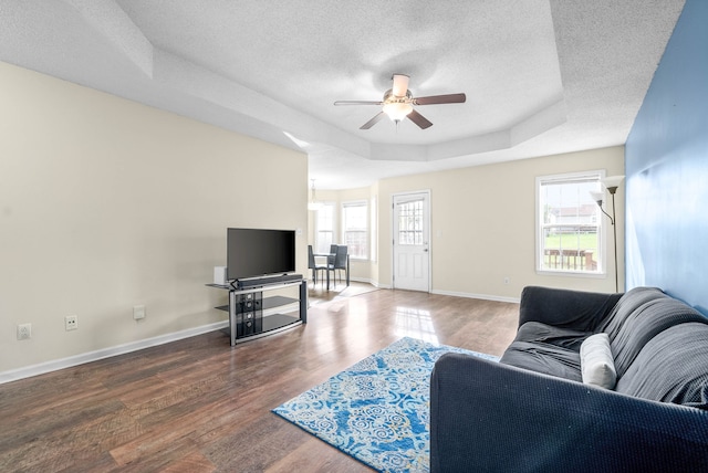 living room featuring hardwood / wood-style flooring, ceiling fan, a raised ceiling, and a textured ceiling