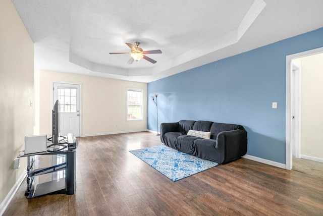 living room with a tray ceiling, ceiling fan, and dark wood-type flooring