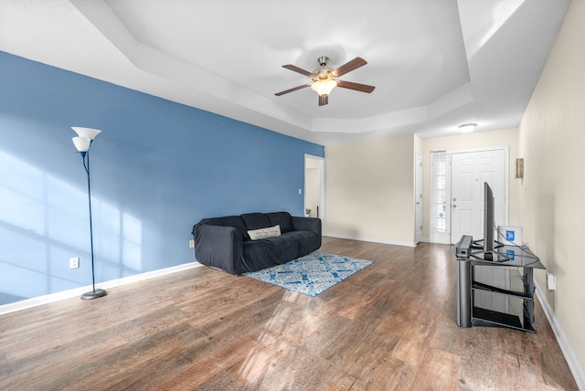 living room featuring a tray ceiling, ceiling fan, and wood-type flooring