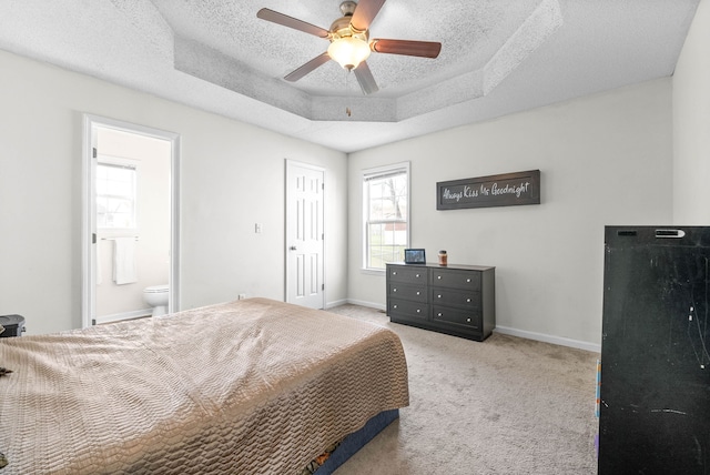 bedroom with ensuite bath, ceiling fan, light colored carpet, a textured ceiling, and a tray ceiling