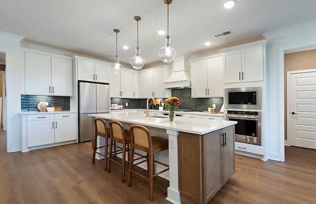 kitchen featuring a center island with sink, appliances with stainless steel finishes, custom exhaust hood, and white cabinets