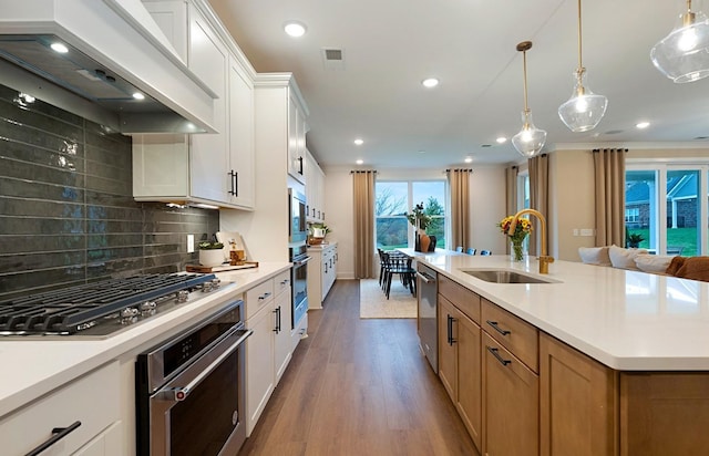 kitchen with pendant lighting, custom exhaust hood, sink, white cabinetry, and appliances with stainless steel finishes