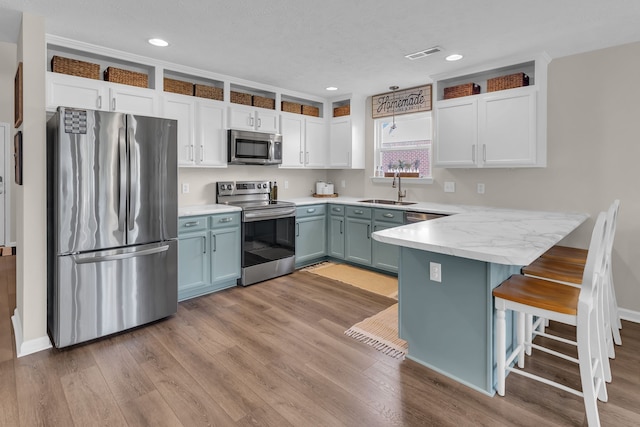 kitchen with a kitchen bar, stainless steel appliances, white cabinetry, and light hardwood / wood-style flooring