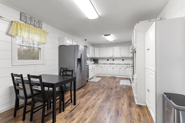 kitchen with white cabinets, dark hardwood / wood-style floors, stainless steel fridge with ice dispenser, and wooden walls