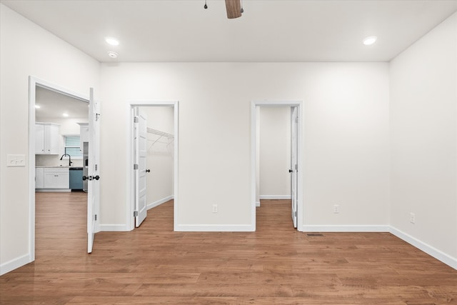 unfurnished bedroom with a walk in closet, sink, ceiling fan, light hardwood / wood-style floors, and a closet