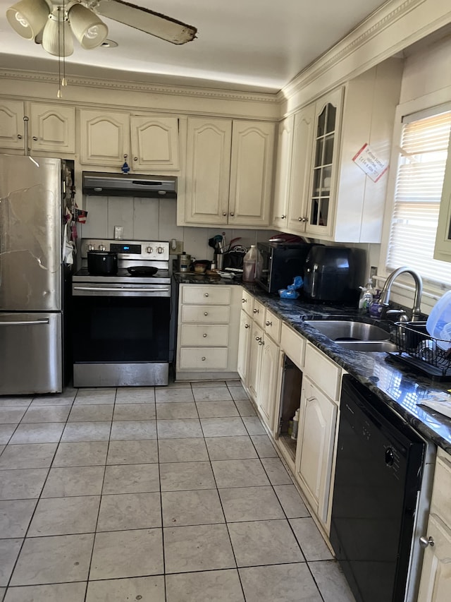 kitchen with sink, dark stone countertops, cream cabinets, light tile patterned floors, and appliances with stainless steel finishes