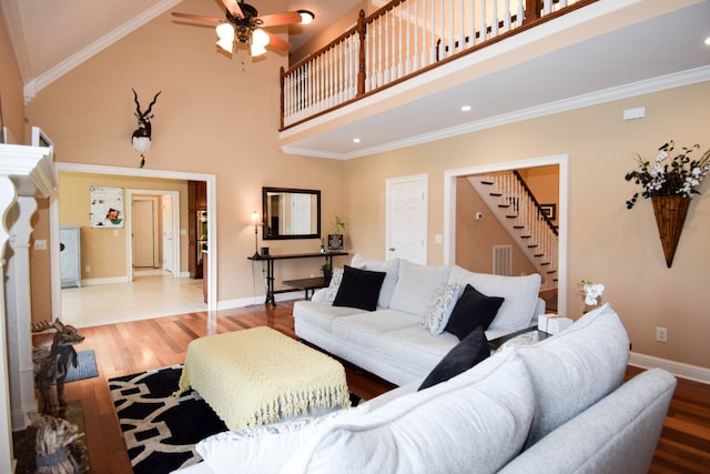 living room featuring a towering ceiling, ceiling fan, ornamental molding, and light hardwood / wood-style floors