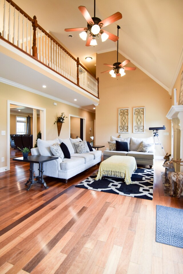 living room with high vaulted ceiling, hardwood / wood-style floors, ornamental molding, and ceiling fan