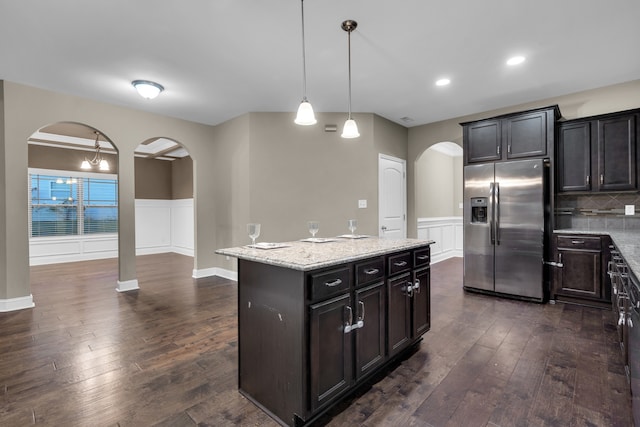 kitchen featuring dark wood-type flooring, light stone counters, stainless steel refrigerator with ice dispenser, decorative light fixtures, and a kitchen island