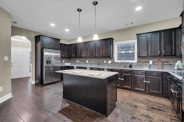 kitchen with light stone countertops, stainless steel refrigerator with ice dispenser, a center island, and hanging light fixtures