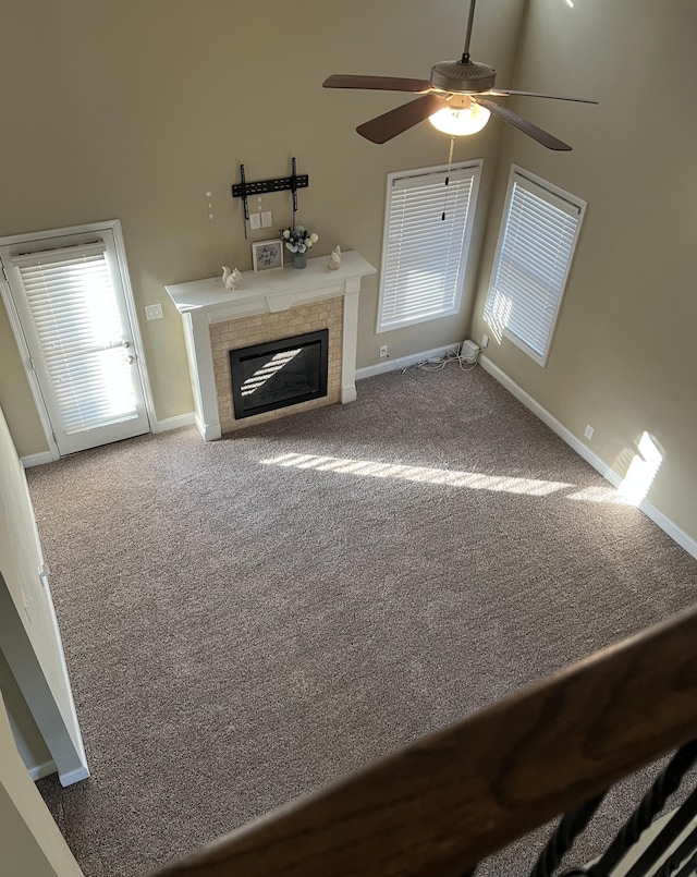 unfurnished living room with ceiling fan, a fireplace, carpet floors, and a high ceiling