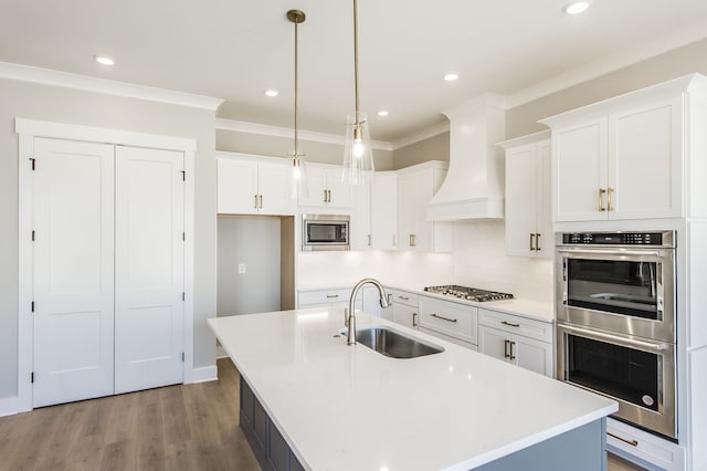 kitchen featuring sink, hanging light fixtures, an island with sink, custom range hood, and stainless steel appliances