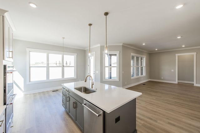 kitchen featuring dishwasher, sink, light hardwood / wood-style floors, decorative light fixtures, and a kitchen island with sink