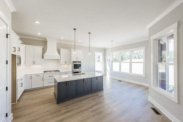 kitchen featuring pendant lighting, a center island with sink, white cabinets, custom range hood, and light wood-type flooring