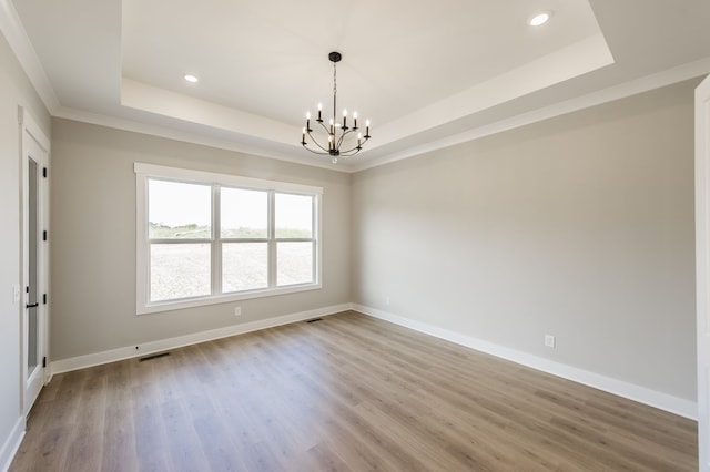 spare room with wood-type flooring, a raised ceiling, a notable chandelier, and crown molding