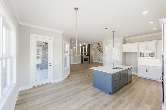 kitchen with a kitchen island with sink, light wood-type flooring, appliances with stainless steel finishes, decorative light fixtures, and white cabinetry