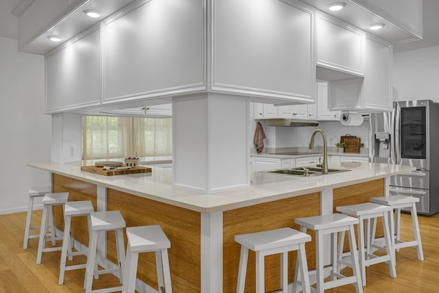 kitchen with sink, white cabinetry, light hardwood / wood-style floors, kitchen peninsula, and a breakfast bar area