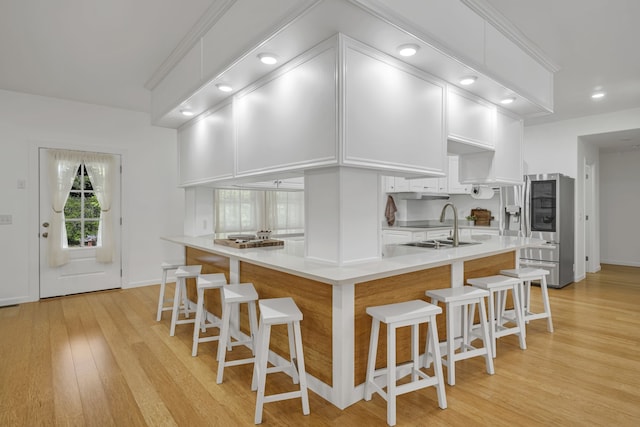 kitchen with sink, a kitchen island, light hardwood / wood-style floors, a kitchen bar, and white cabinets