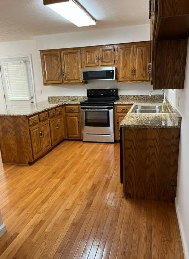 1159 New Hope Rd, Celina, TN 38551 - kitchen featuring stainless steel appliances, a sink, a peninsula, light wood-style floors, and brown cabinets