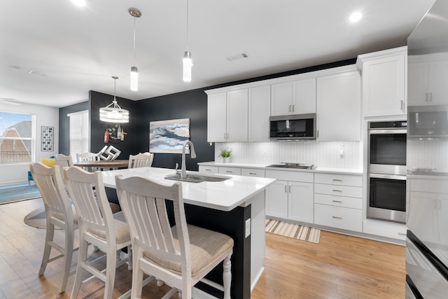 kitchen with stainless steel appliances, tasteful backsplash, pendant lighting, white cabinets, and sink