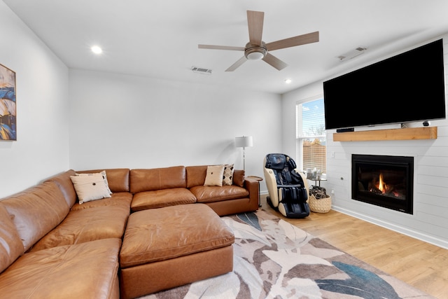 living room with ceiling fan, a large fireplace, and wood-type flooring