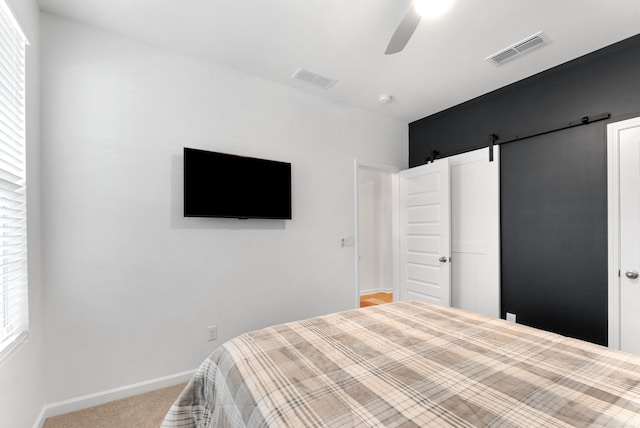 carpeted bedroom with ceiling fan, a barn door, and multiple windows