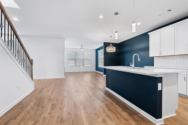 kitchen featuring white cabinetry, sink, backsplash, hanging light fixtures, and a center island with sink