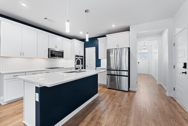 kitchen with pendant lighting, appliances with stainless steel finishes, white cabinetry, decorative backsplash, and a kitchen island with sink