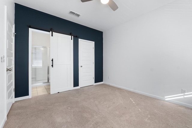 unfurnished bedroom featuring ceiling fan, light colored carpet, and a barn door