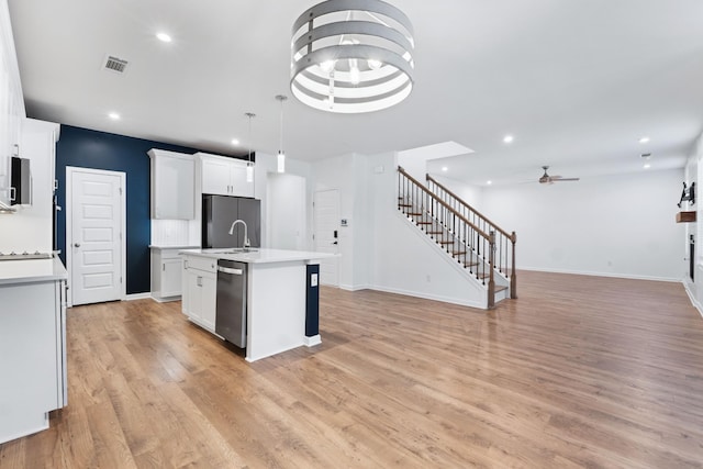 kitchen with decorative light fixtures, ceiling fan, a center island with sink, appliances with stainless steel finishes, and white cabinets