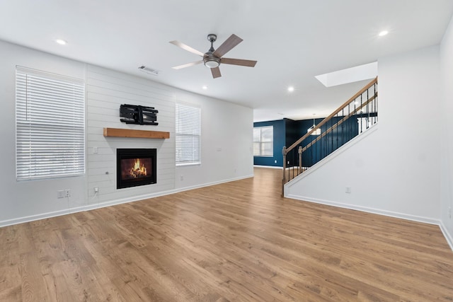 unfurnished living room featuring hardwood / wood-style flooring, a large fireplace, and ceiling fan