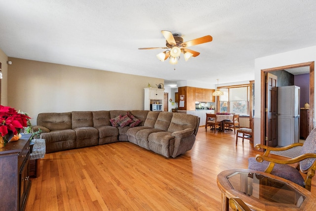 living room featuring ceiling fan, light wood-type flooring, and a textured ceiling