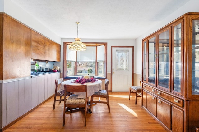 dining space featuring a textured ceiling, light hardwood / wood-style flooring, and wooden walls