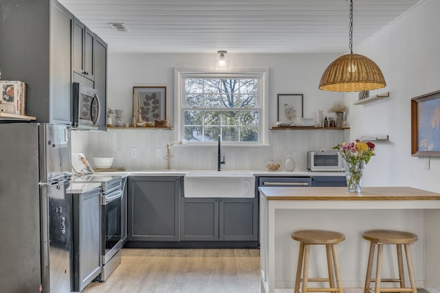 kitchen with gray cabinetry, sink, stainless steel appliances, a breakfast bar area, and light wood-type flooring