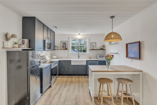 kitchen featuring appliances with stainless steel finishes, a breakfast bar, sink, decorative light fixtures, and light hardwood / wood-style flooring