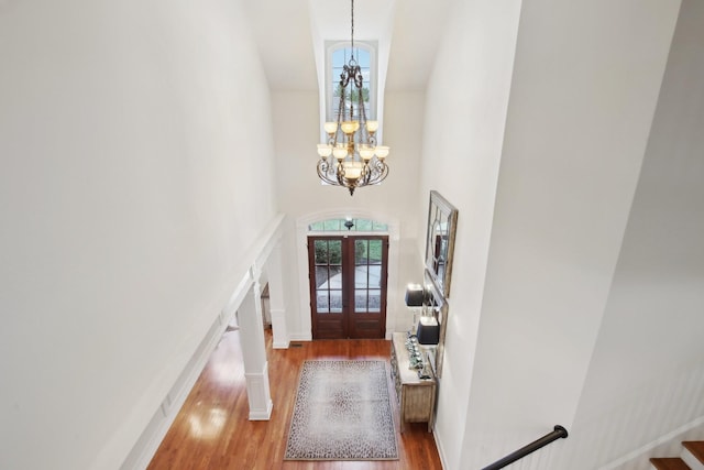 foyer with an inviting chandelier, a towering ceiling, wood-type flooring, and french doors