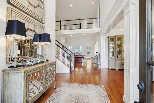 foyer entrance featuring decorative columns, wood-type flooring, and a high ceiling