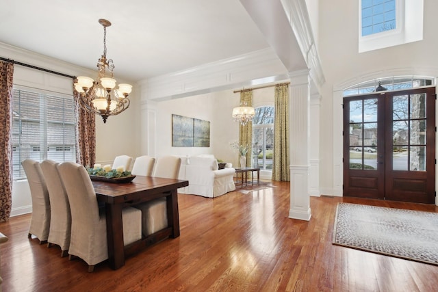 dining area with wood-type flooring, a chandelier, and ornate columns