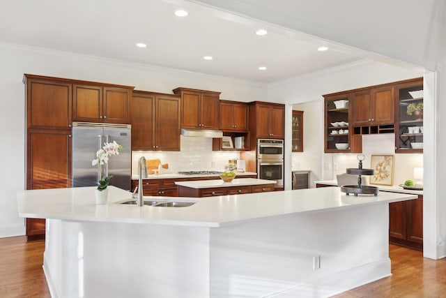 kitchen featuring sink, light wood-type flooring, appliances with stainless steel finishes, a kitchen island with sink, and decorative backsplash