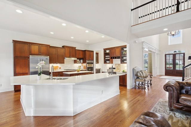 kitchen with a spacious island, sink, light wood-type flooring, appliances with stainless steel finishes, and a high ceiling