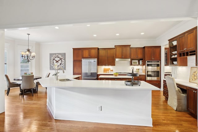 kitchen with pendant lighting, stainless steel appliances, sink, and an island with sink