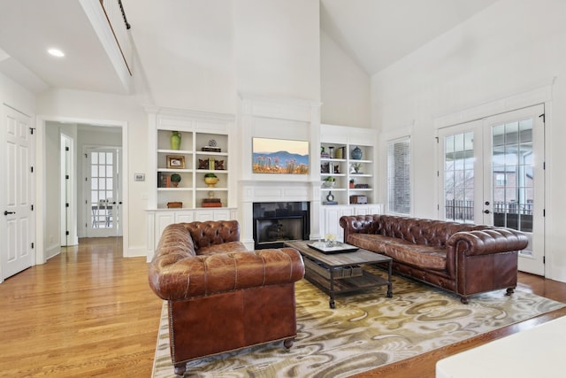 living room featuring french doors, built in shelves, high vaulted ceiling, and light hardwood / wood-style flooring