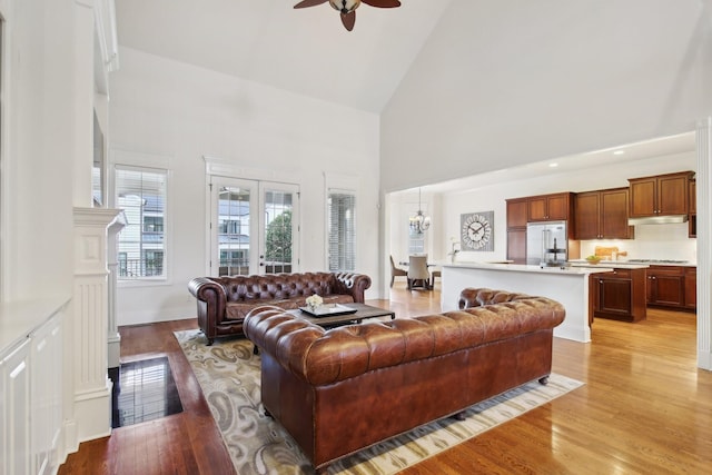 living room with high vaulted ceiling, ceiling fan with notable chandelier, and light wood-type flooring