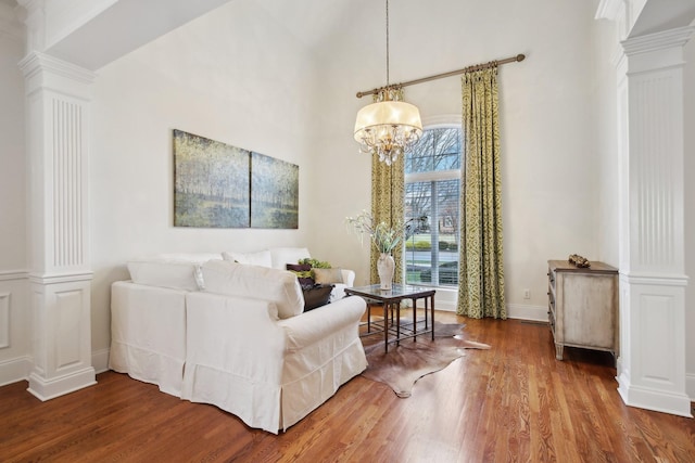 living room with a notable chandelier, hardwood / wood-style flooring, a high ceiling, and ornate columns